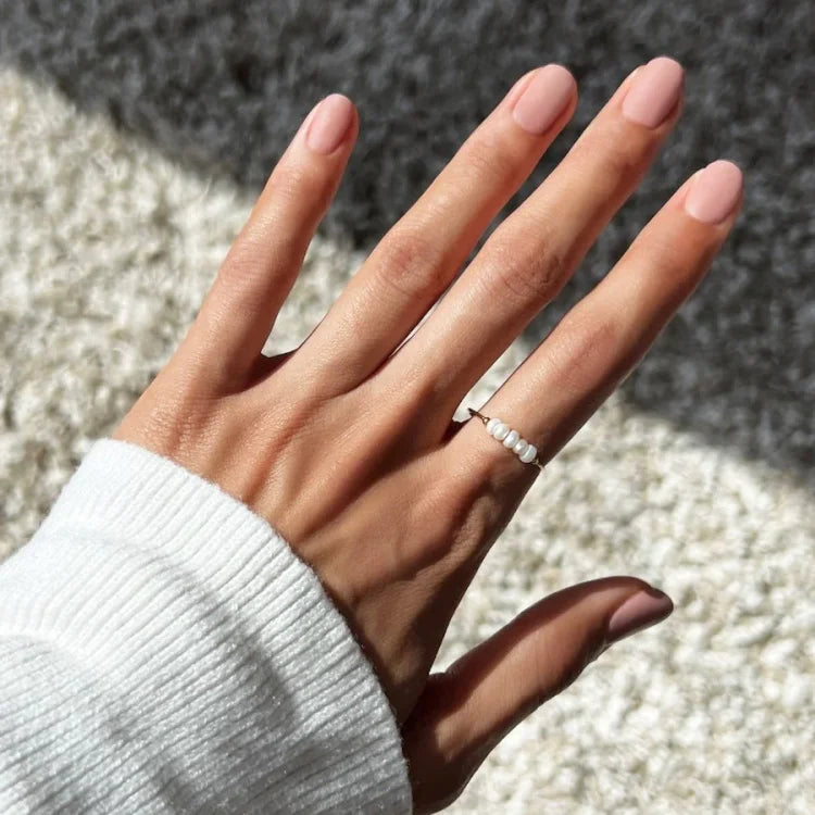 Hand mit weißem Perlenring auf Teppich, Damenmode, Schmuck, elegantes Accessoire.