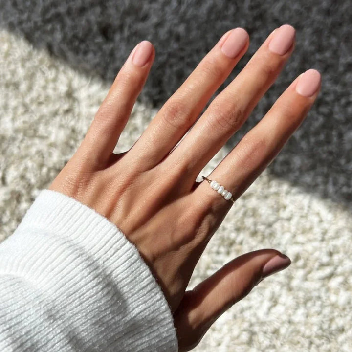 Hand mit weißem Perlenring auf Teppich, Damenmode, Schmuck, elegantes Accessoire.