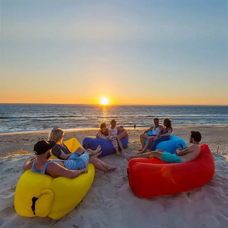 Personen entspannen auf bunten Luftsofas am Strand bei Sonnenuntergang.