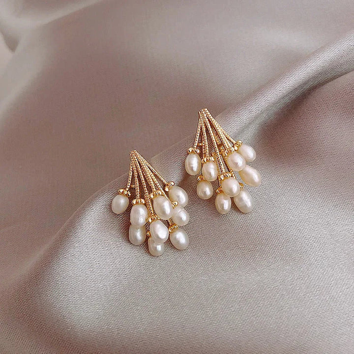 Goldene Ohrringe mit weißen Perlen auf beigem Satin, eleganter Schmuck für Damen.