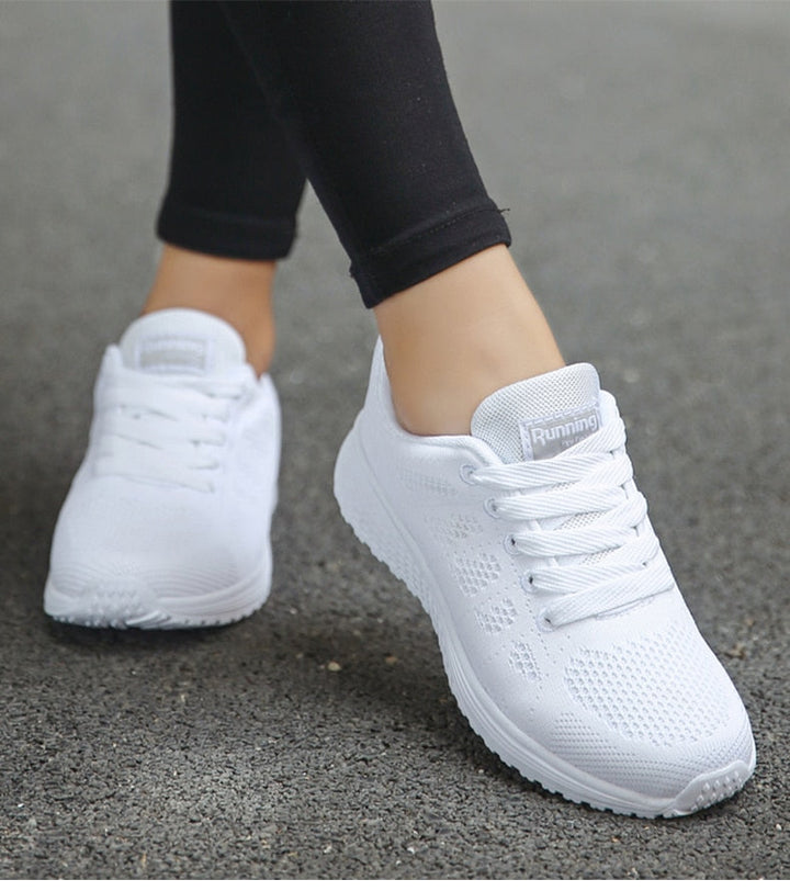 Weiße Damen-Laufschuhe, atmungsaktiv, mit Schnürsenkeln, auf Asphalt getragen.