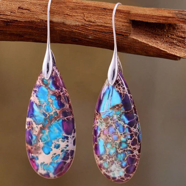 Bunte Tropfen-Ohrringe aus Harz, lila und blau, an Ast hängend, modisches Schmuckdesign.