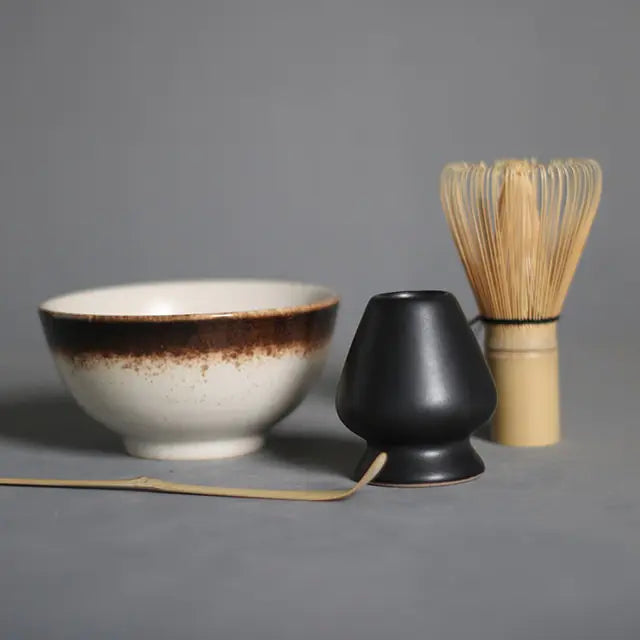 Matcha-Set mit Schale, schwarzem Halter und Bambusbesen auf grauem Hintergrund.