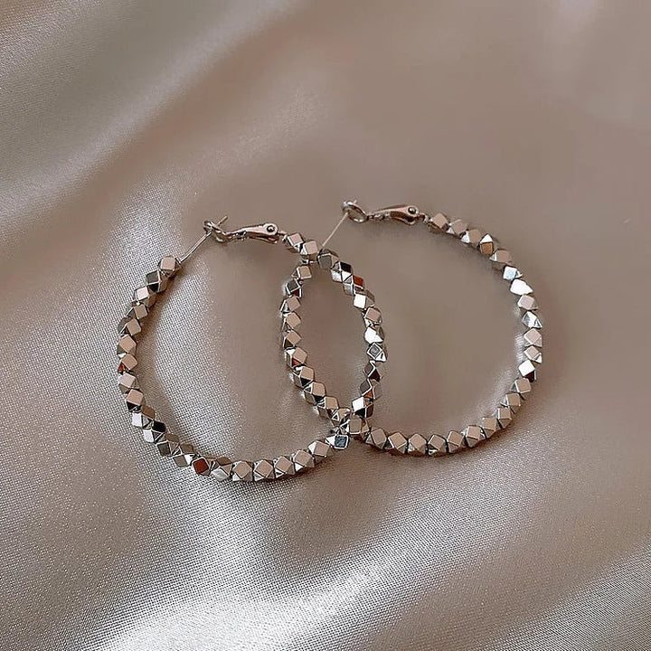 Silberne Creolen Ohrringe, facettierte Oberfläche, eleganter Schmuck auf Satin-Hintergrund.
