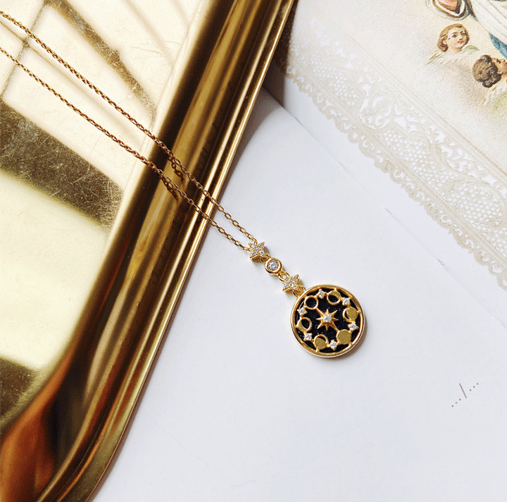 Goldene Halskette mit schwarzem, sternförmigem Anhänger auf Tablett, eleganter Schmuck.