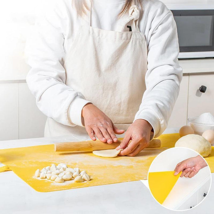 Person rollt Teig auf gelber Silikon-Backmatte in Küche, mit Nudelholz und Mehl.