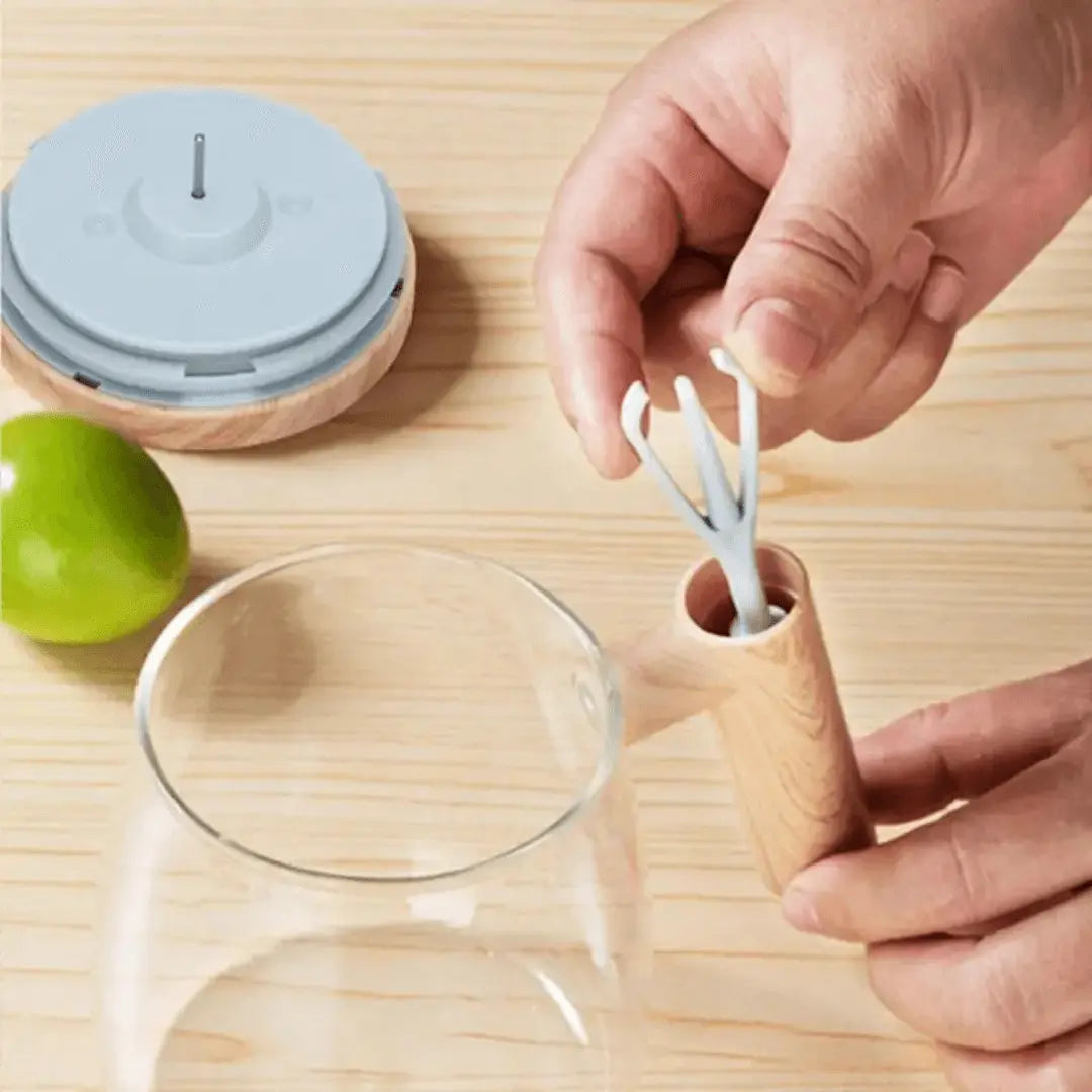 Hand hält Holzgriff mit grauem Silikonaufsatz, Glas und Limette auf Holztisch.