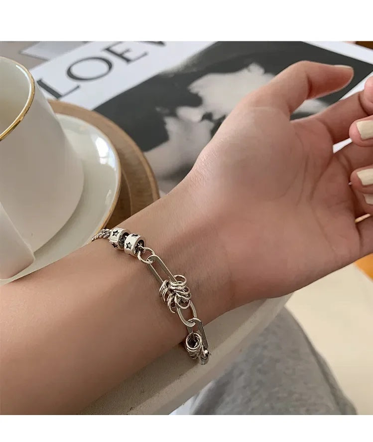 Silberarmband mit Sternenmotiv auf Handgelenk, neben weißer Tasse auf Tisch.