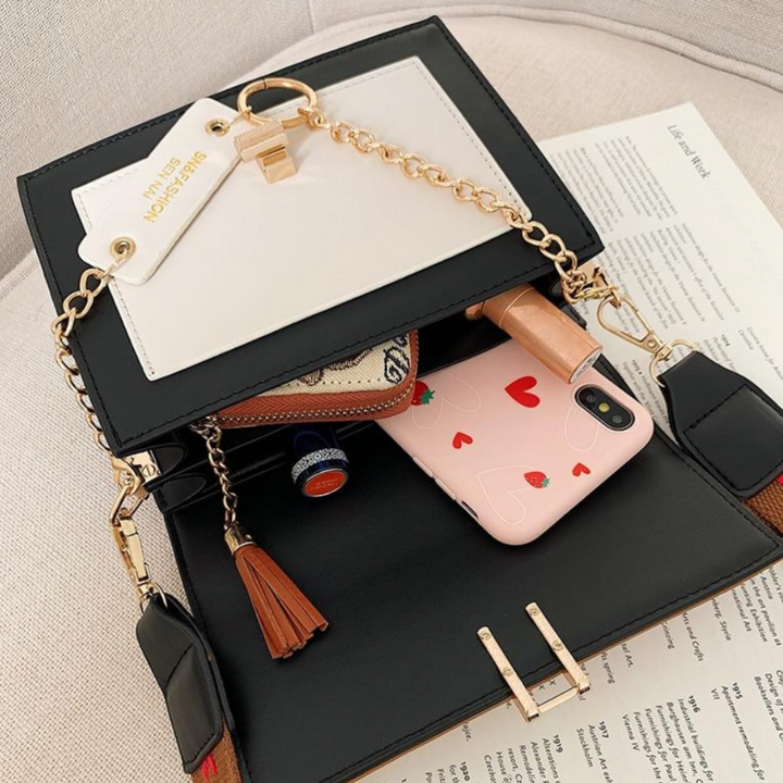Schwarze Handtasche mit goldener Kette, Leder, enthält Smartphone und Kosmetikartikel.