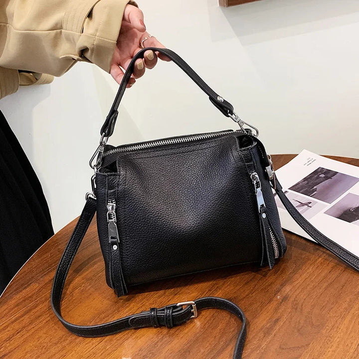 Schwarze Lederhandtasche mit Reißverschlüssen auf Holztisch, modisch und elegant.