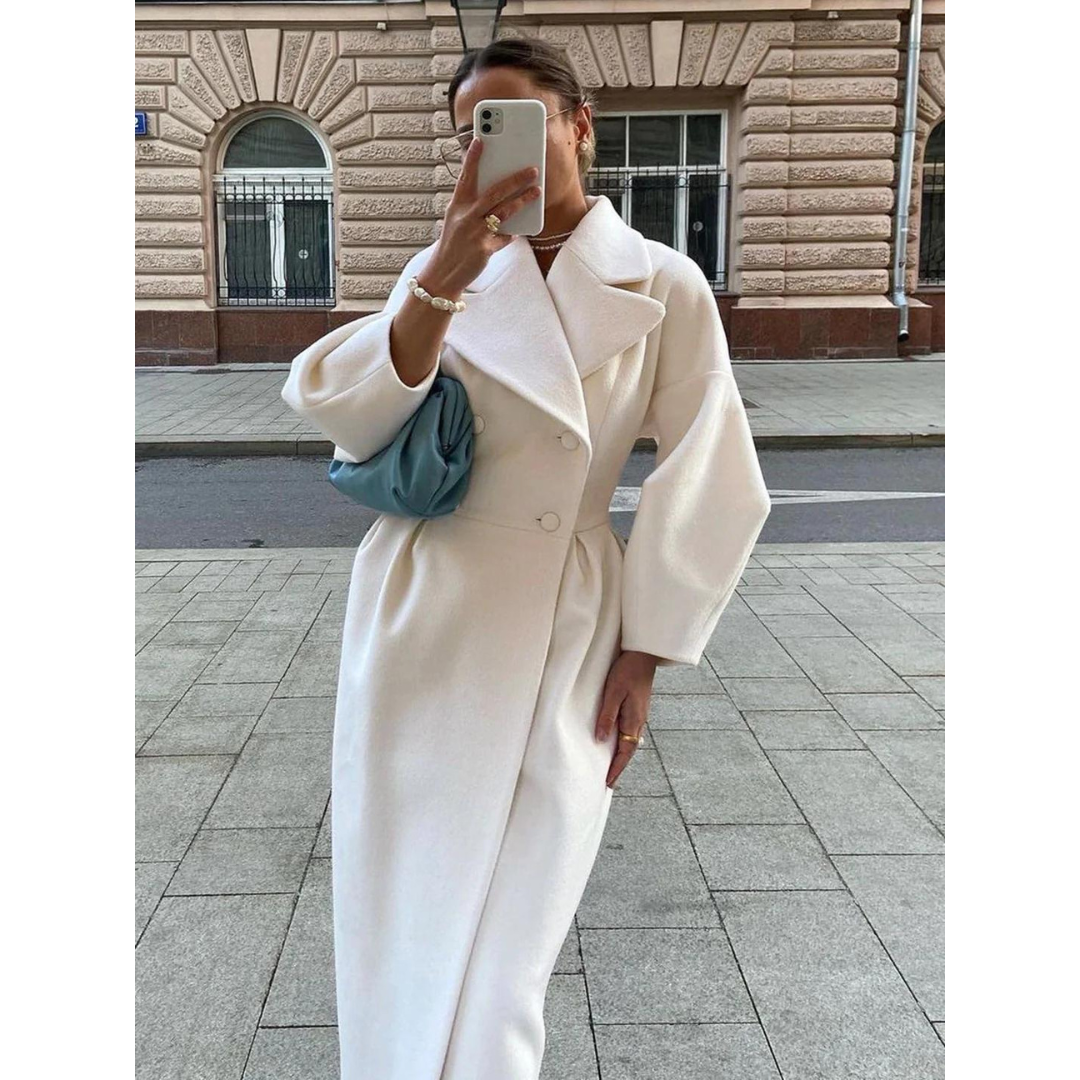 Frau in weißem Wollmantel mit blauer Tasche, fotografiert auf städtischer Straße.