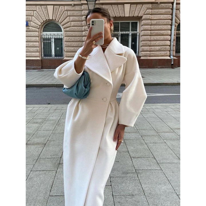 Frau in weißem Wollmantel mit blauer Tasche, fotografiert auf städtischer Straße.