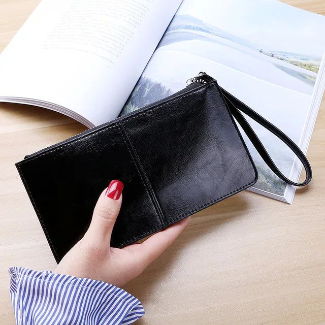 Schwarze Lederhandtasche mit Handgelenkschlaufe, elegante Damenmode, auf Holztisch.