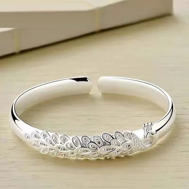 Silberarmreif mit Pfauenmotiv, elegantes Design, Schmuck für Damen, modisches Accessoire.