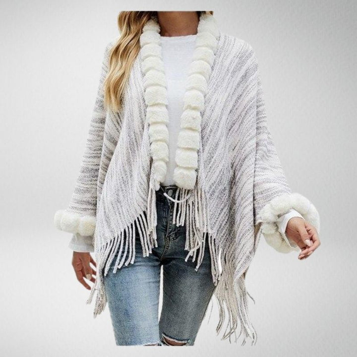 Frau in grauem Strickponcho mit Fransen und weißem Kunstfell, lässige Mode.