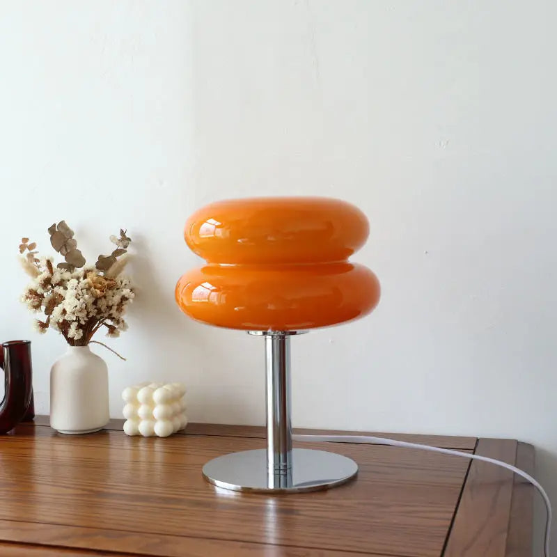 Orangefarbene Tischlampe aus Glas auf Holztisch, moderne Inneneinrichtung, Metallfuß.