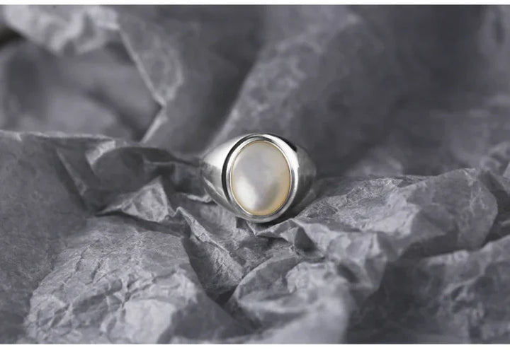 Silberring mit Perlmuttstein auf grauem Hintergrund, eleganter Schmuck für Damen.