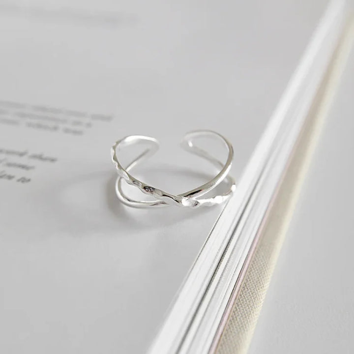 Silberner, verstellbarer Ring mit elegantem, gedrehtem Design auf weißem Hintergrund.