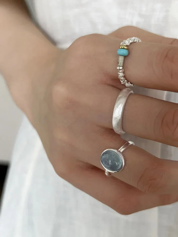Hand mit drei Silberringen, einer mit blauem Stein, auf weißem Hintergrund.