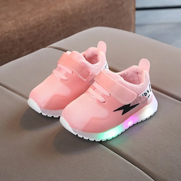 Rosa LED-Kinderschuhe mit Klettverschluss, Blitz-Design, auf grauem Sofa.