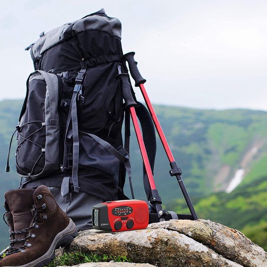 Schwarzer Wanderrucksack, rote Trekkingstöcke, braune Wanderschuhe auf Felsen in Berglandschaft.