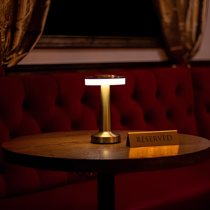 Goldene Tischlampe auf Holztisch, modernes Design, LED-Beleuchtung, rotes Sofa im Hintergrund.