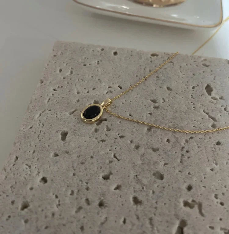 Goldene Halskette mit schwarzem Anhänger auf Steinplatte, eleganter Schmuck, minimalistisch.