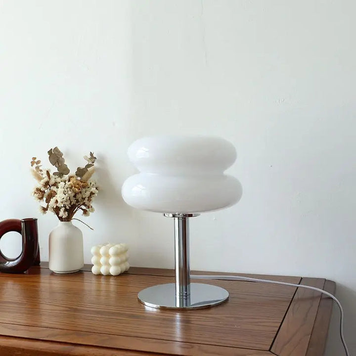 Moderne weiße Tischlampe aus Glas auf Holztisch, dekoriert mit Trockenblumen und Kerzen.