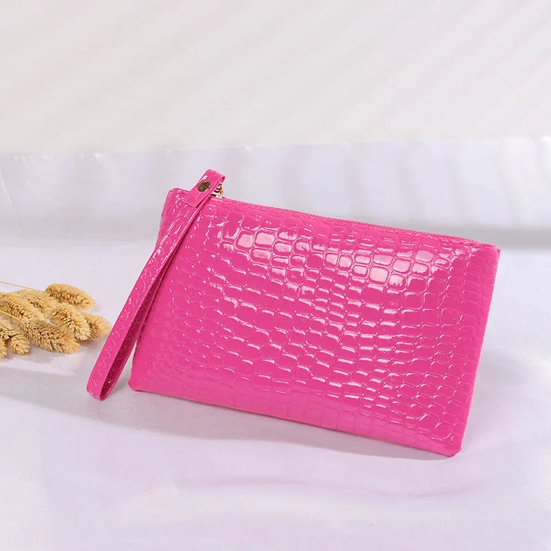 Rosa glänzende Krokodilleder-Clutch mit Reißverschluss und Trageschlaufe auf weißem Hintergrund.
