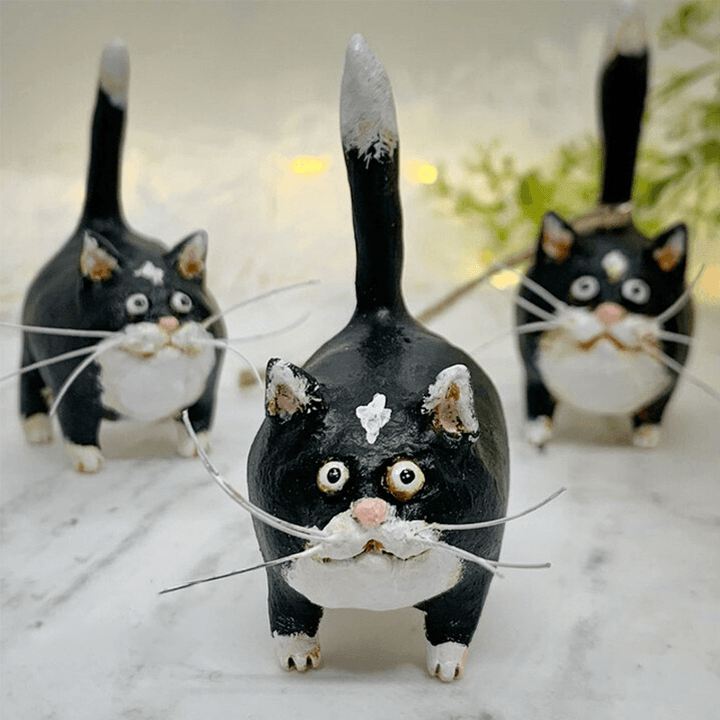 Drei handgefertigte schwarze Katzenfiguren aus Keramik mit weißen Details auf Marmortisch.