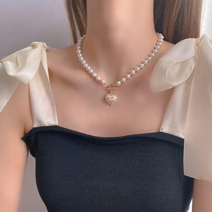 Frau mit Perlenkette und Herzanhänger, schwarzes Top, elegante Modeaccessoires.
