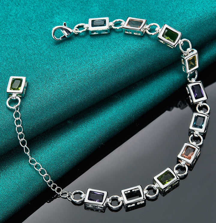 Silberarmband mit bunten Edelsteinen auf grünem Stoff, eleganter Schmuck, Damenaccessoire.