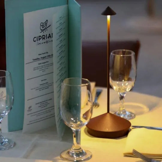 Tischlampe LED modern, bronzefarben, neben Weingläsern und Speisekarte im Restaurant.