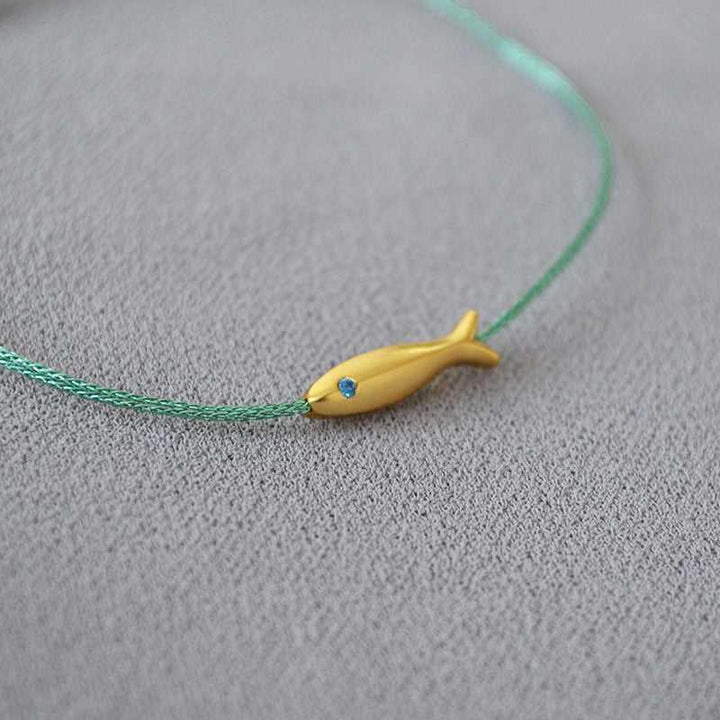 Goldener Fischanhänger auf grünem Armband, minimalistisches Schmuckdesign, Geschenkidee.