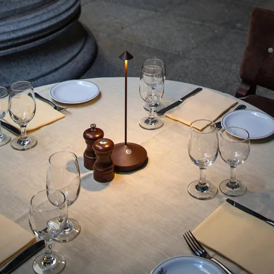 Runder Esstisch mit Tischlampe, Weingläsern, Tellern und Salz-Pfeffer-Streuer, elegant gedeckt.