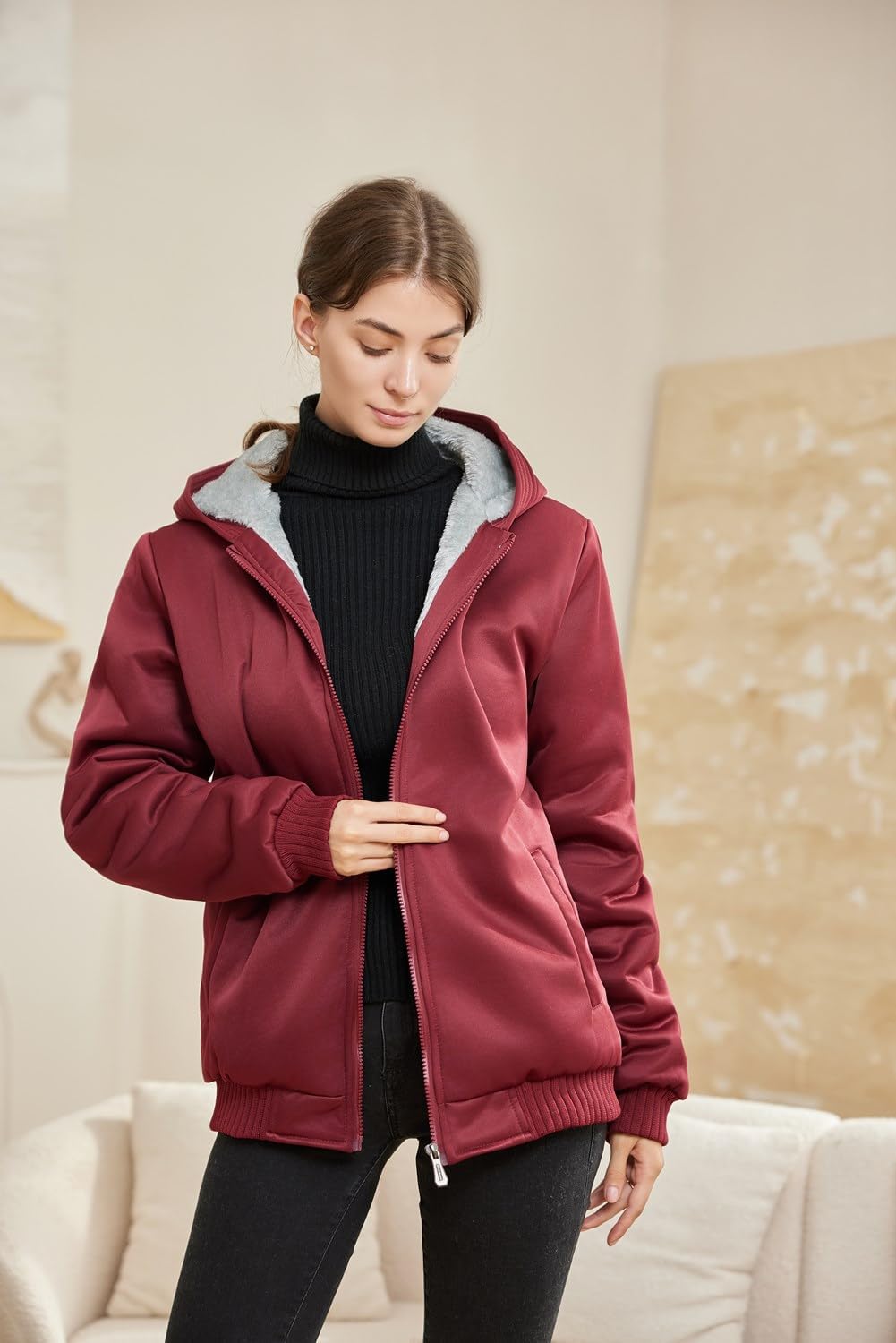 Frau in roter Kapuzenjacke, schwarzem Rollkragenpullover, gemütliche Wintermode, Innenaufnahme.