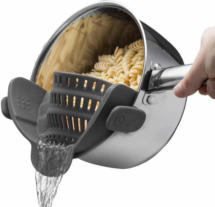 Hand hält Edelstahlkochtopf mit Nudeln, Wasser wird durch schwarzen Silikonsieb abgegossen.