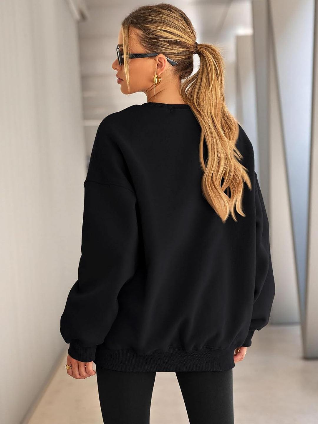 Frau in schwarzem Oversize-Pullover und Sonnenbrille, lässiger Look, blonde Haare, modern.