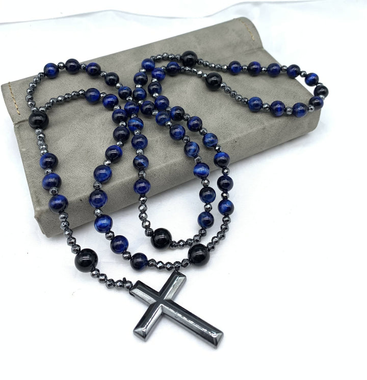 Blau-schwarze Perlenkette mit silbernem Kreuzanhänger auf grauem Hintergrund, modisches Accessoire.