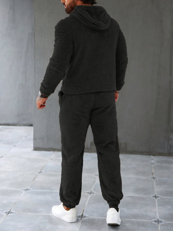 Mann in schwarzem Fleece-Trainingsanzug, Kapuze, weiße Sneaker, Rückansicht.