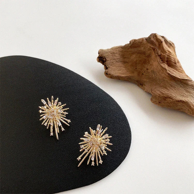 Goldene Sonnenstrahl-Ohrringe auf schwarzem Leder, eleganter Schmuck, modernes Design.