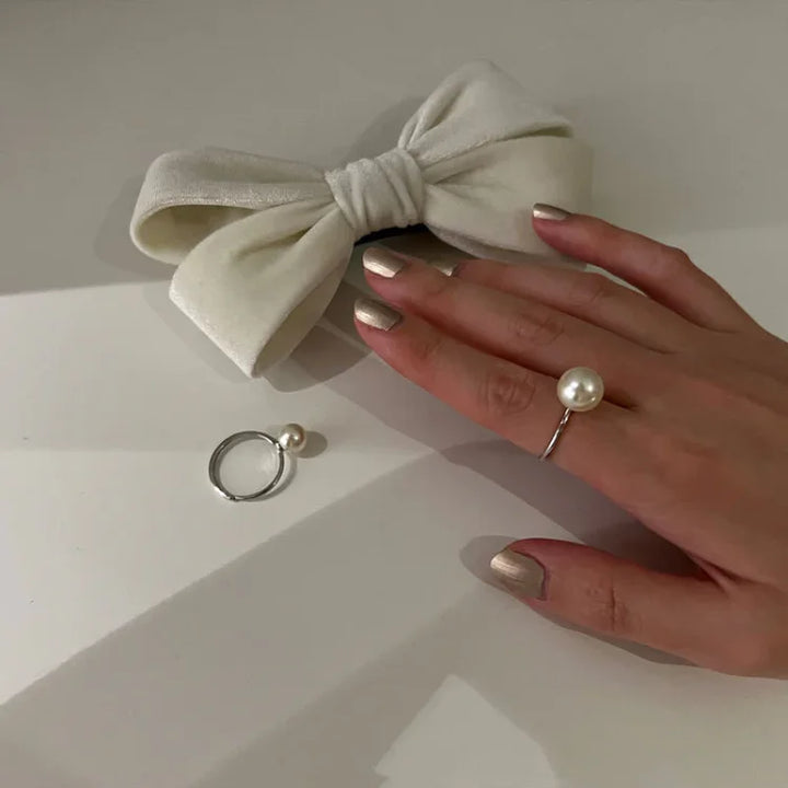 Perlenring an Hand mit weißer Schleife, eleganter Schmuck, Damenmode, Accessoire, stilvoll.