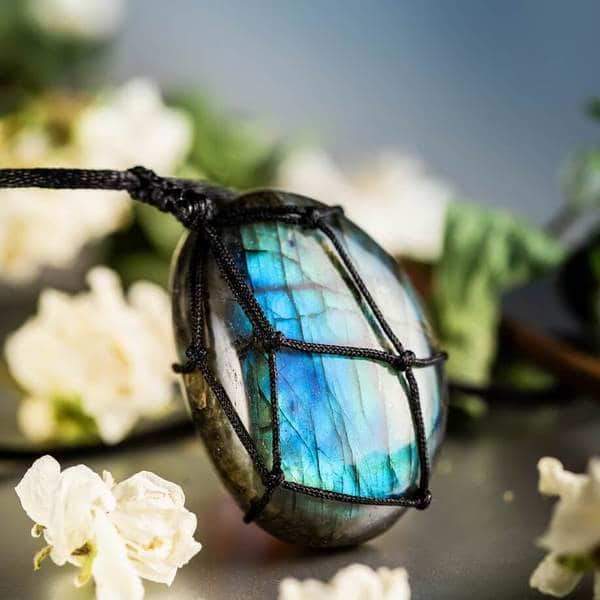 Labradorit-Anhänger mit schwarzem Band, umgeben von weißen Blumen, Schmuck, Edelstein, Geschenk.