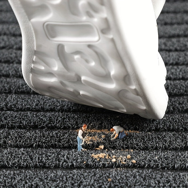 Weiße Sneaker-Sohle auf schwarzer Fußmatte, Miniaturfiguren reinigen Schmutz.