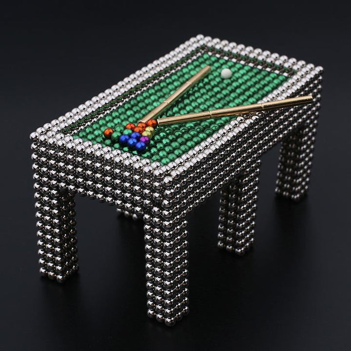Miniatur-Billardtisch aus Magnetkugeln, grün, mit Queues und Kugeln, auf schwarzem Hintergrund.