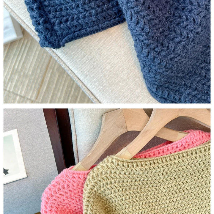 Dunkelblauer, rosa und gelber Strickpullover auf Holzkleiderbügeln auf einem Sofa.