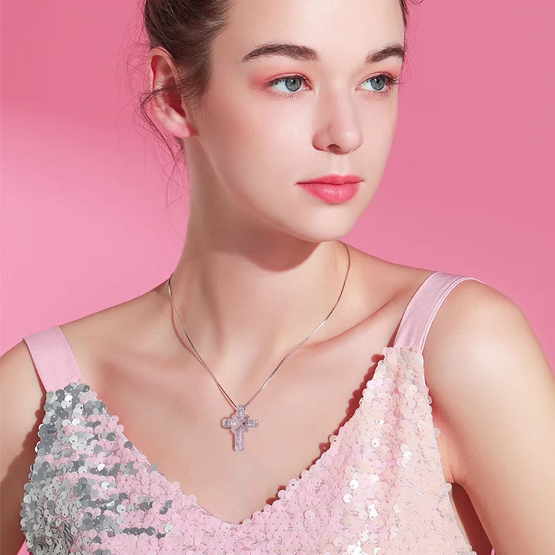Frau mit rosa Paillettenkleid und Kreuzanhänger vor rosa Hintergrund.