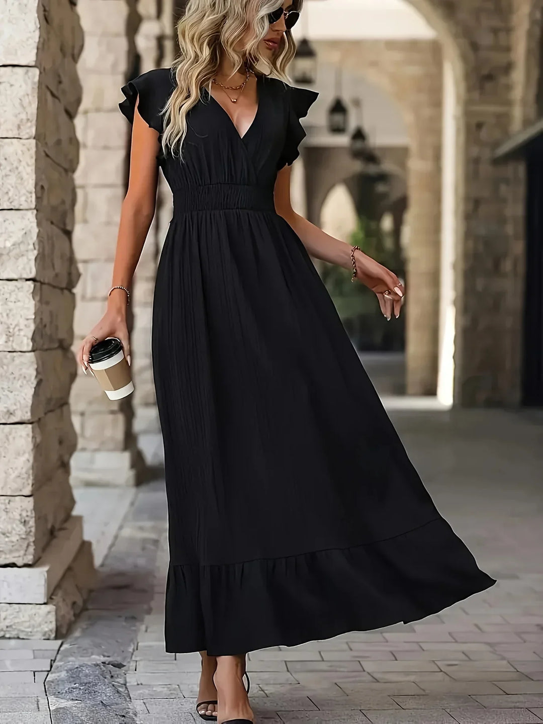 Frau in schwarzem Maxikleid mit Kaffeebecher, elegante Mode, Sommerkleid, Stadtbummel.