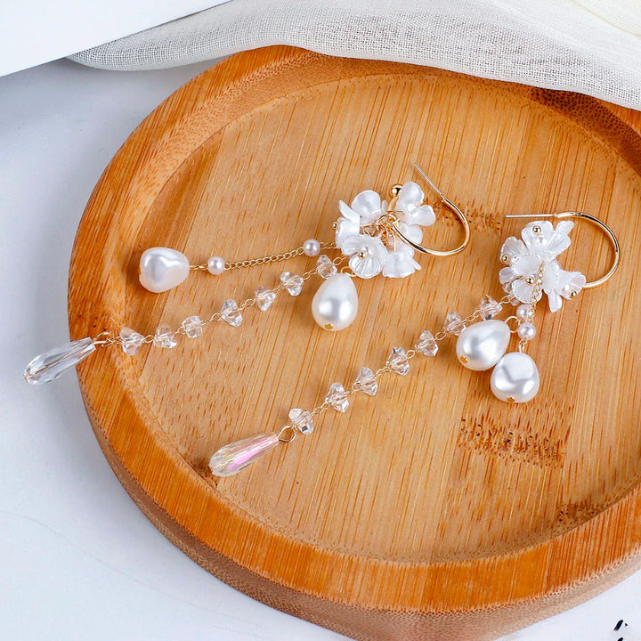 Goldene Ohrringe mit Perlen und Kristallen auf Bambusteller, eleganter Schmuck für Damen.