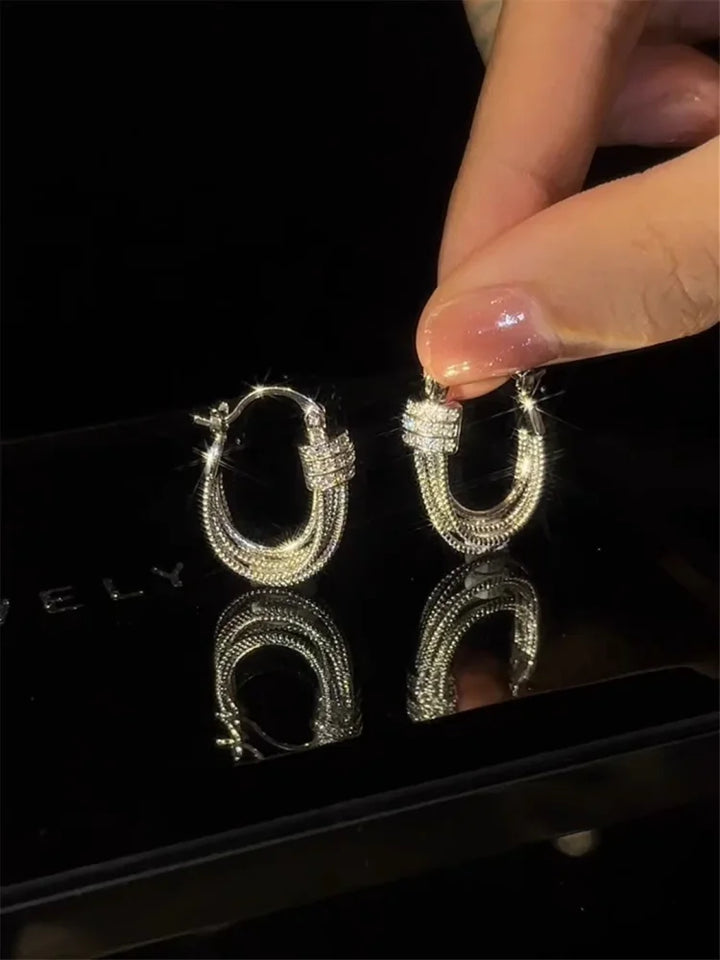Silberne Creolen-Ohrringe mit Strasssteinen, glänzend, eleganter Schmuck, Hand hält Ohrring.